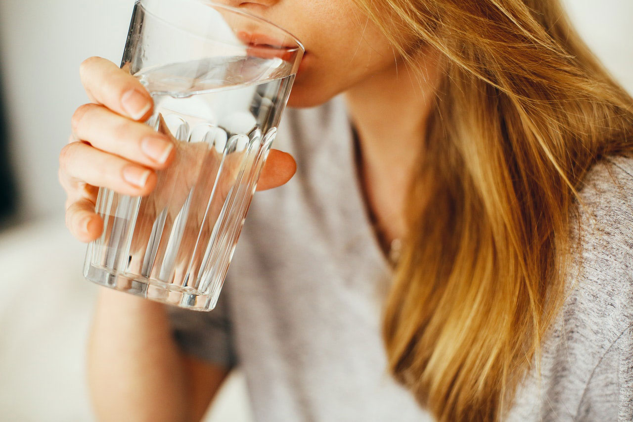 Frau mit blonden langen Haaren trinkt Wasser aus einem Glas.